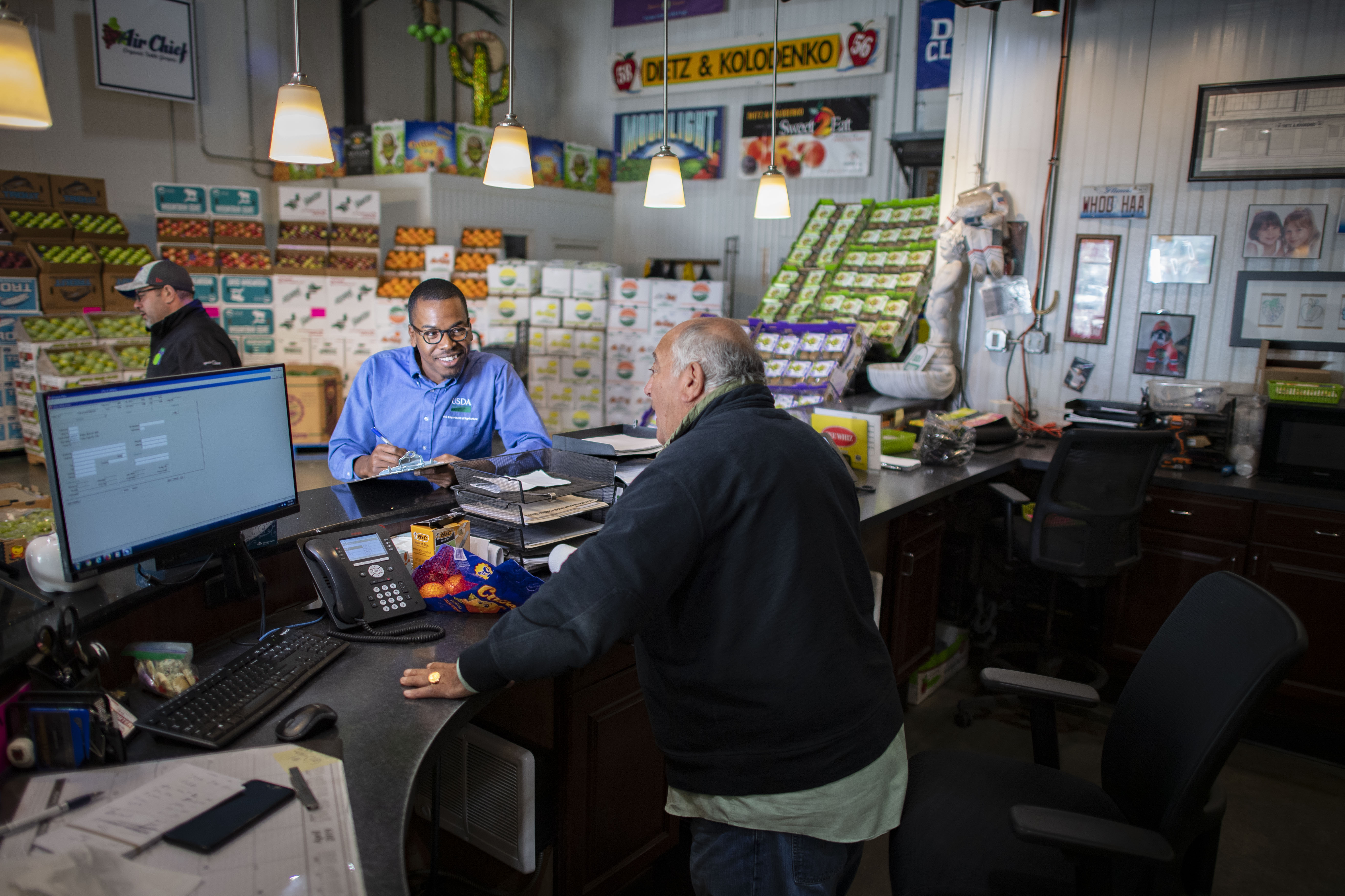 USDA employee talking to a man behind the counter in a fruit market