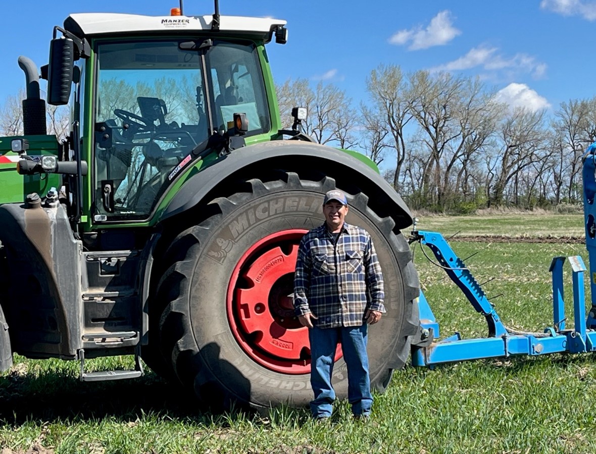 Man standing in front of wheel of tractor in a field